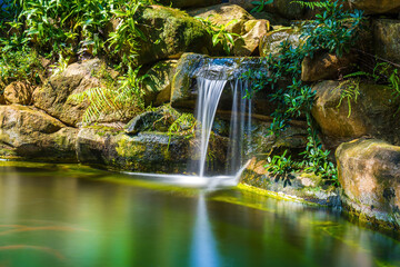 Japanese garden waterfalls. Lush green tropical Koi pond with waterfall from each side. A lush green garden with waterfall cascading down the rocky stones. Zen and peaceful background.