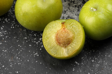 Canvas Print - Small mini green fresh juicy plum fruit in wooden bowl on black slate stone board wooden table cut slice half seed sprinkled salt