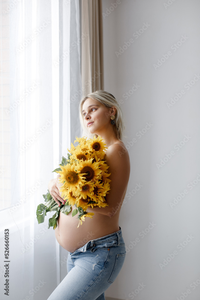 A pregnant woman with a naked belly and jeans covers her body with a