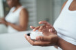 © gpointstudio - Young African-American  woman about to apply face cream in the mirror reflection.