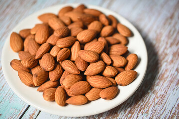 Wall Mural - Almonds nuts on white palte, Delicious sweet almonds on the wooden table background, roasted almond nut for healthy food and snack