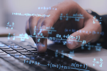 Close up of businessman hands using laptop keyboard at workplace with monitor, supplies and glowing mathematical formulas on blue background. Education, knowledge and statistics concept.