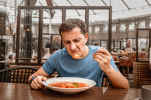 Dissatisfied Unhappy Customer Of The Restaurant Sniffs The Disgusting Smell Of A Bowl Of Soup With Spoiled Ingredients And Is Going To Complain To The Chef