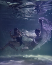 Fashionable Man And Woman In Glasses Underwater On A Dark Blue Background In The Pool