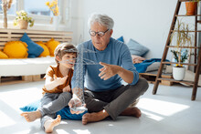 Grandson And Grandfather Examining Electricity Pylon Model In Living Room