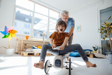 Happy Grandfather Pushing Grandson Sitting On Toy Car At Home