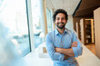 © Westend61 - Happy man with arms crossed in library