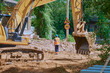 © Алексей Игнатов - Yellow crawler excavator at a road reconstruction site in a village with old log houses. Summer sunny day.