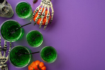 Halloween night party concept. Top view photo of green swamp punch with floating spiders straws skull skeleton hands holding pumpkin and insects on isolated violet background with copyspace