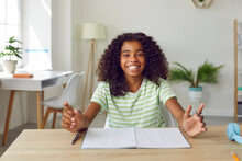 Happy School Child Sitting At Desk At Home. Portrait Of Cheerful African American Student Girl At Table Looking At Camera And Smiling. Online Class, Videocall Or Videoconference Laptop PC Screen View