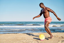 Black Man Kicking Ball On Beach