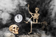 Halloween time. A skeleton crawling out of a tomb, a skull, a clock on a black, smoky, dusty background. The eve of the day of death.