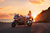 World Motorcyclist Day. Caucasian young woman lying posing on a motorcycle. Golden sunset and ocean on the background. Freedom and motorcycle trips