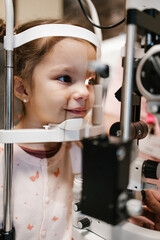 Wall Mural - Beautiful and adorable little girl receiving ophthalmology treatment. Doctor ophthalmologist checking her eyesight with modern equipment.