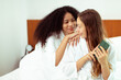 © Jade - Caucasian and black women love together and lying on bed as diversity person. Young Adult Romantic couple check smart phone behind her back for secret chat text as jealous feeling, copy space