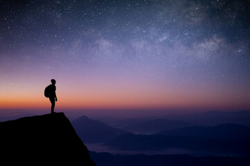 Wall Mural - Silhouette of young traveler with backpack standing and watched the star, milky way and night sky alone on top of the mountain. He enjoyed traveling and was successful when he reached the summit.