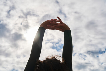 Woman wearing wetsuit stretching at the open air with cloudy sky at the background