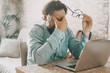 © simona - Tired man holding glass and touching is eyes after over work on notebook computer. Online activity and problems to solve concept. Modern worker people using laptop at table desk. Economy difficulty