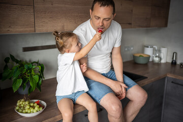 Wall Mural - Cute little girl and her handsome dad are eating fruit in modern kitchen. Healthy eating.