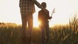 © Acronym - Farmer and his son in front of a sunset agricultural landscape. Man and a boy in a countryside field. Fatherhood, country life, farming and country lifestyle.