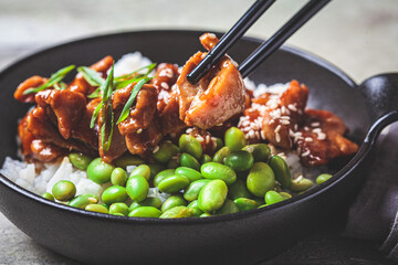 Wall Mural - Teriyaki chicken with rice , onion and edamame beans in black bowl.