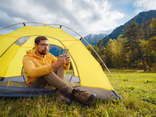 Wall Mural - trip to Caucasus mountains, Arkhyz, Teberdinsky reserve. Man traveler relaxing in mountains in tent camping outdoor , uses app on smartphone. Travel adventure lifestyle concept hiking active vacations