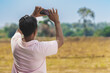 © JinnaritT - Back view of Asian man using cell phone to take sky photo in field. Taking photo on mobile phone of sky view. Male take picture of the landscape with his smartphone on cloudy day. Outdoor happiness.
