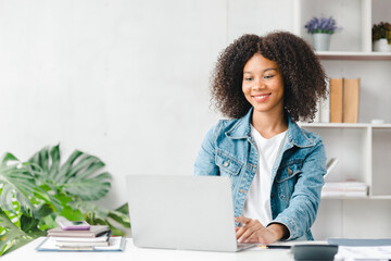 American teenage woman sitting in white office with laptop, she is a student studying online with laptop at home, university student studying online, online web education concept.