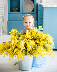 little smiing blond cute girl  in blue dress sitting in blue and white kitchen with yellow flowers mimosa 