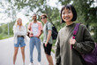 © LIGHTFIELD STUDIOS - brunette asian woman with backpack looking at camera near blurred multicultural friends.