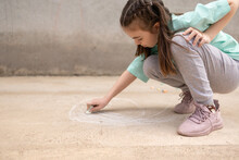 Girl Draws With Colorful Crayons On Pavement. Children's Drawings With Chalk On Wall. Creative Kid