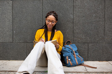 Wall Mural - Smiling young african american student sitting outside writing in book