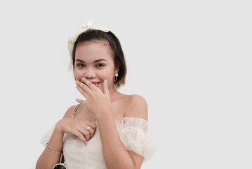 Wall Mural - A petite woman wearing a white off shoulder lace and a bow on her hair covers her mouth looking shy isolated on a white background.
