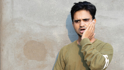 Wall Mural - Tooth ache concept. Indoor shot of young male feeling pain, holding his cheek with hand, suffering from bad toothache, looking at camera with painful expression