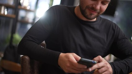 happy young man holding smartphone device browsing internet online seated. portrait face and hand cl