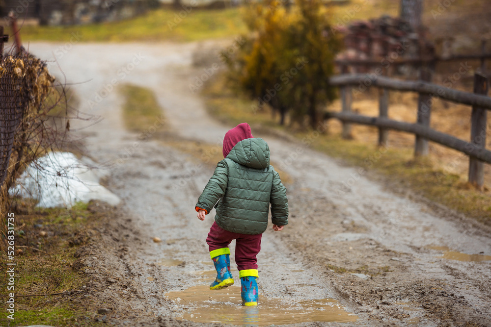 Little boy in protective rubber boots and rain clothes jumping in mud ...