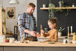 © Mediaphotos - Little boy helping his dad to decorate vegetable salad with cheese at table in domestic kitchen