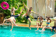 © yurakrasil - Group of happy six friends drinking jumping in pool day party with splash