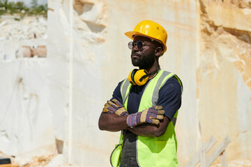 Aufkleber - Young African American worker in coveralls, reflective vest, black t-shirt, gloves and yellowprotective helmet standing at marble quarry