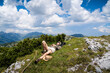 © macondos - young Caucasian woman lying down and taking a rest in the grass on a mountain peak with blue sky and clouds above