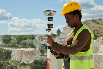 Aufkleber - Young serious black woman in workwear and safety helmet adjusting technical equipment for measuring territory of marble quarry