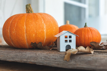 Autumnal Background. Toy house and pumpkin on wooden background. Thanksgiving banner copy space. Hygge mood, change of seasons concept. Hello Autumn with family Halloween party