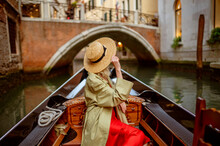 Rear, Back View Of Elegant Woman Wearing Straw Hat On Gondola Ride Along Beautiful Street In Venice, Italy. Travel, Vacation, Lifestyle Conception. Copy, Empty Space For Text