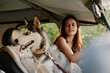 A woman sits in a car with her husky dog ​​and smiles