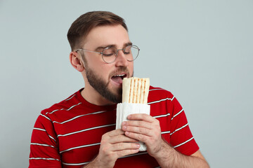 Wall Mural - Young man eating delicious shawarma on grey background