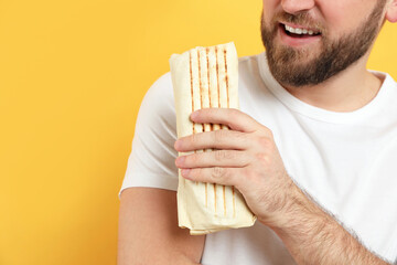 Wall Mural - Young man with delicious shawarma on yellow background, closeup. Space for text