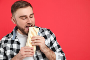 Wall Mural - Young man eating delicious shawarma on red background, space for text