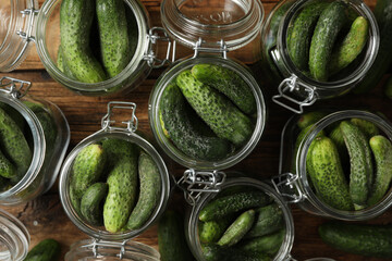 Pickling jars with fresh cucumbers on wooden table, flat lay