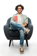 People And Furniture Concept - Happy Smiling Young Man In Glasses With Popcorn Sitting In Chair Over White Background