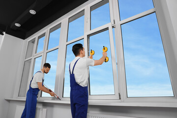 Sticker - Workers with tube of sealant and suction lifters installing plastic windows indoors